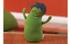 A green, travel-sized stuffed toy resembling an egg with arms and glasses, set against a blurred background.