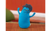 A turquoise, travel-sized stuffed toy resembling an egg with arms and glasses, set against a blurred background.